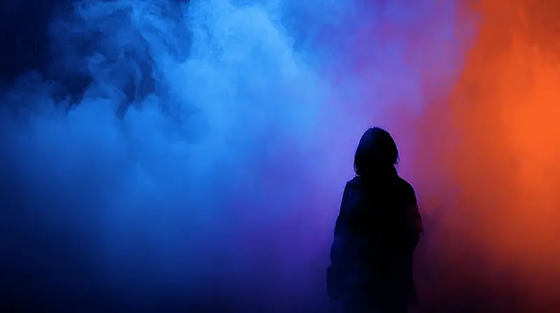 person standing in dark room surrounded by floating colored smoke clouds