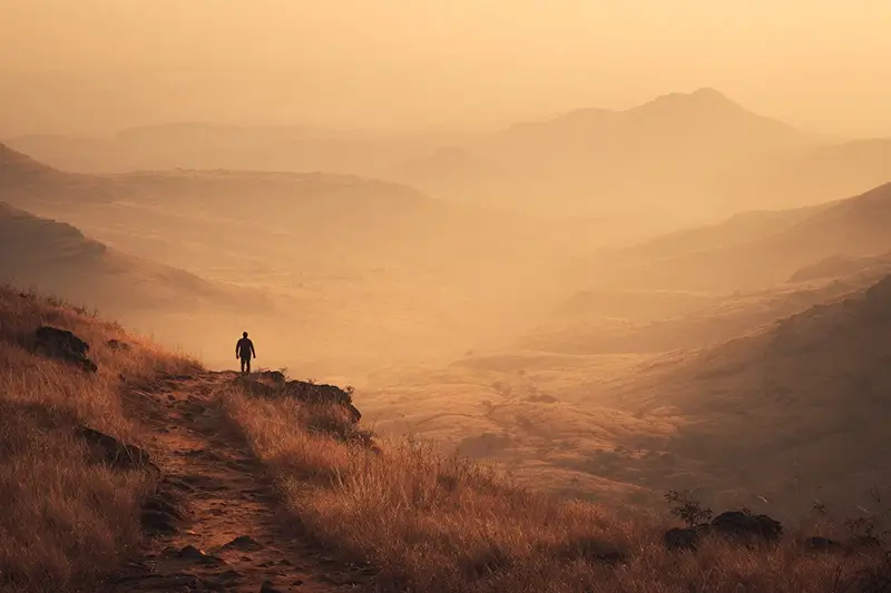 exhausted lone figure standing still on a long mountain trail at sunset