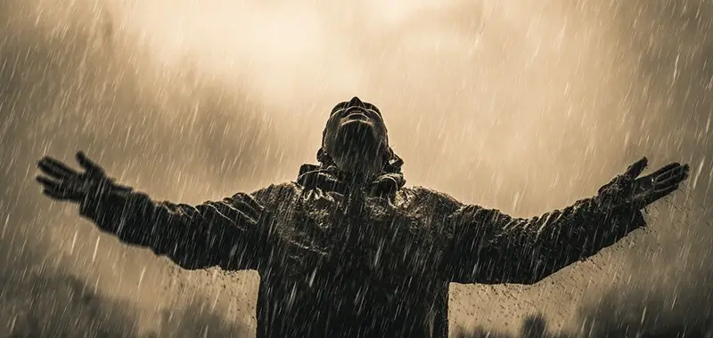 A person standing in the rain with arms open wide, head lifted upward